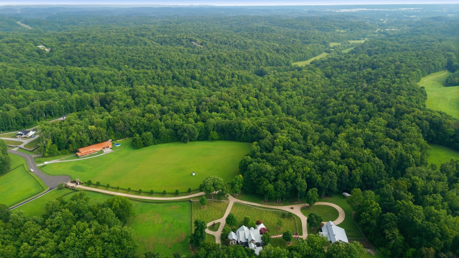 Aerial of the property showing open pasture in front and mature woods rising behind