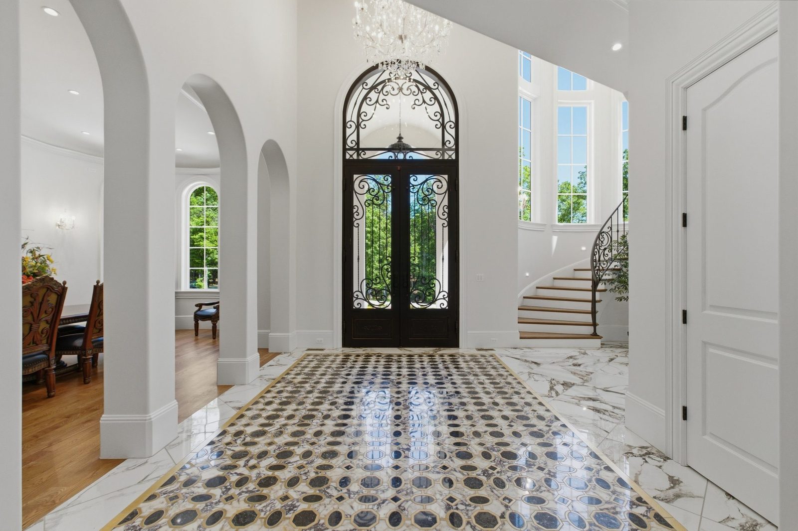 Two story foyer with iron and glass arched doors and a curved staircase